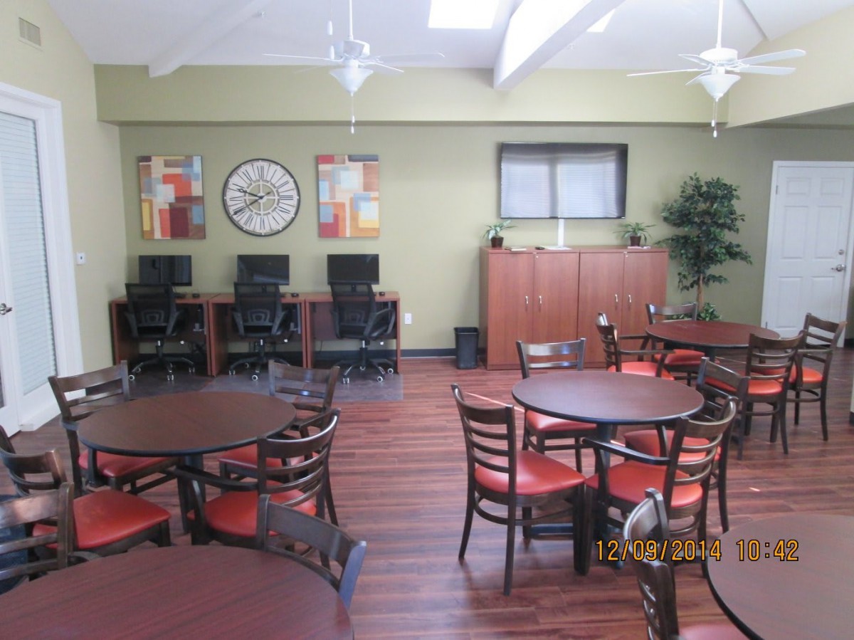 A communal space with dining tables and chairs, computers, and a large wall clock.