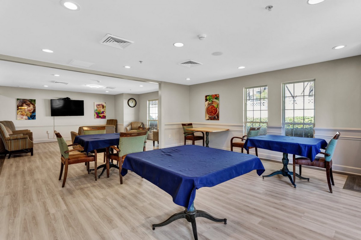 A brightly lit dining area with tables covered in blue tablecloths and chairs arranged neatly on a wooden floor.