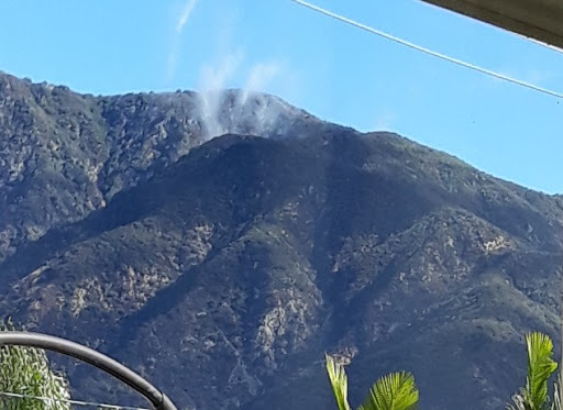 A scenic view of mountains with wisps of smoke against a clear blue sky.