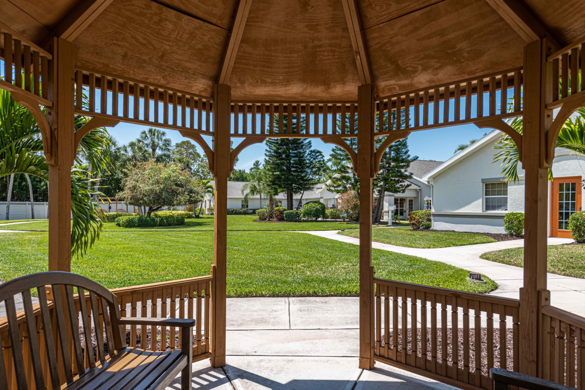 View from inside a wooden gazebo overlooking a lush green lawn and residential homes.