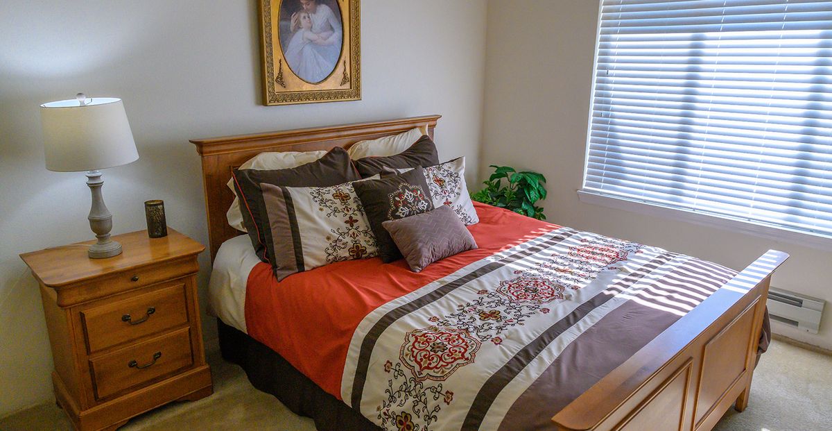 A cozy bedroom with a neatly made bed featuring colorful pillows and bedding, adorned with a portrait on the wall.