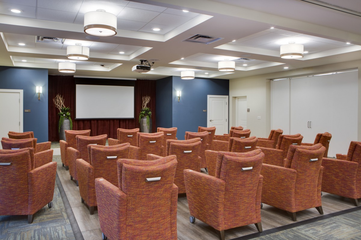 A modern conference room with theater-style seating and a large projector screen.