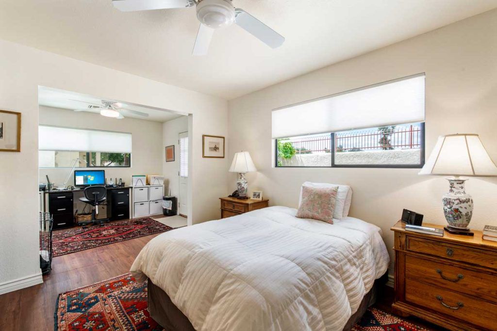 A cozy bedroom with a home office nook, featuring natural light and tasteful decor.