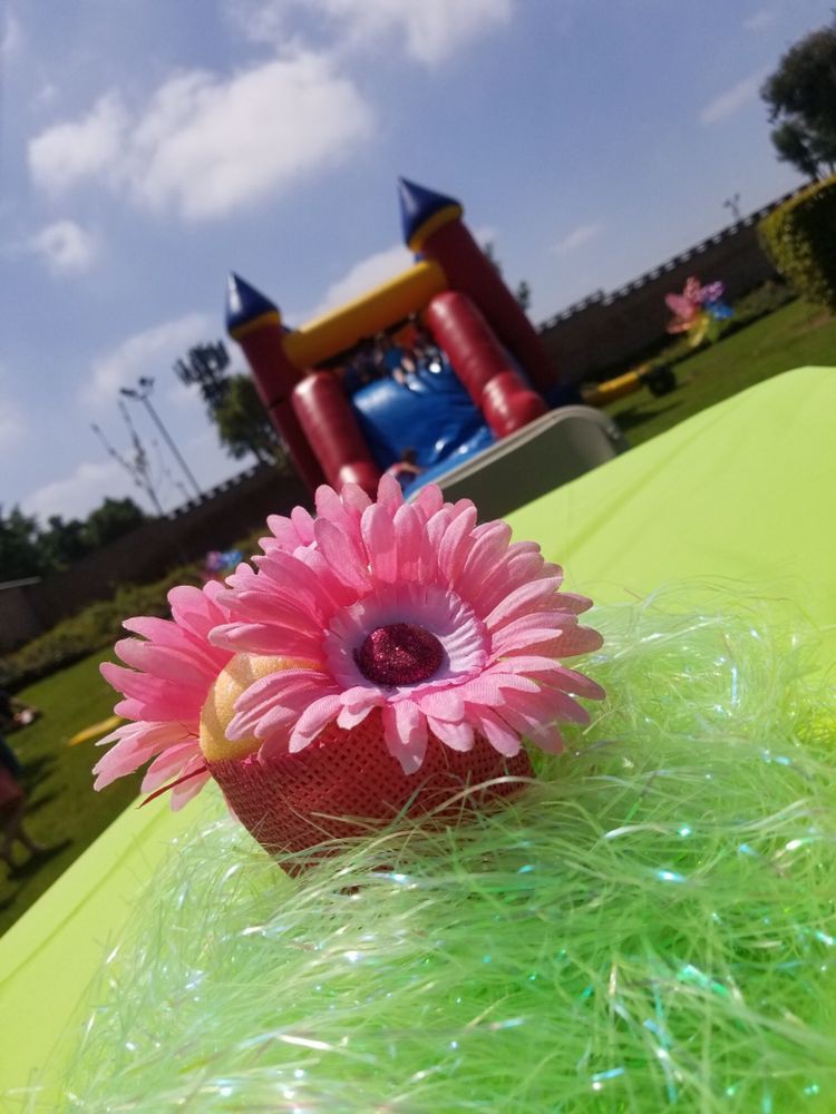A bright outdoor party setup with a colorful flower decoration on the table and a bounce house in the background.