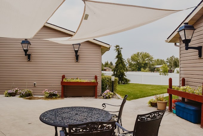 A cozy patio with metal furniture and a shade sail, overlooking a neatly manicured backyard.