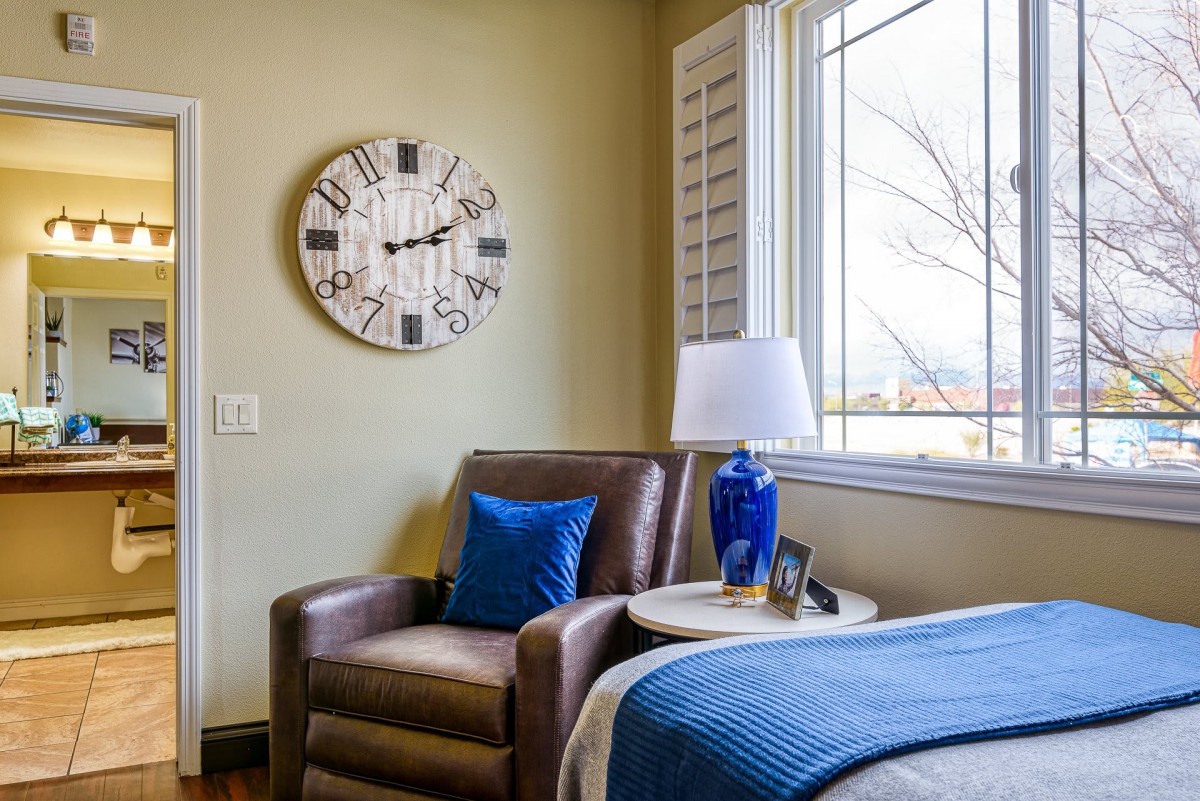 A cozy living room corner with a leather armchair, blue accents, and a large wall clock.