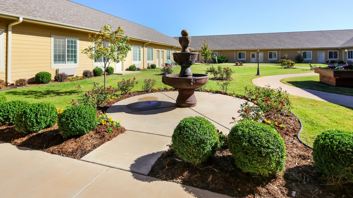 A beautifully landscaped courtyard featuring a central fountain surrounded by neatly trimmed bushes and paved walkways.