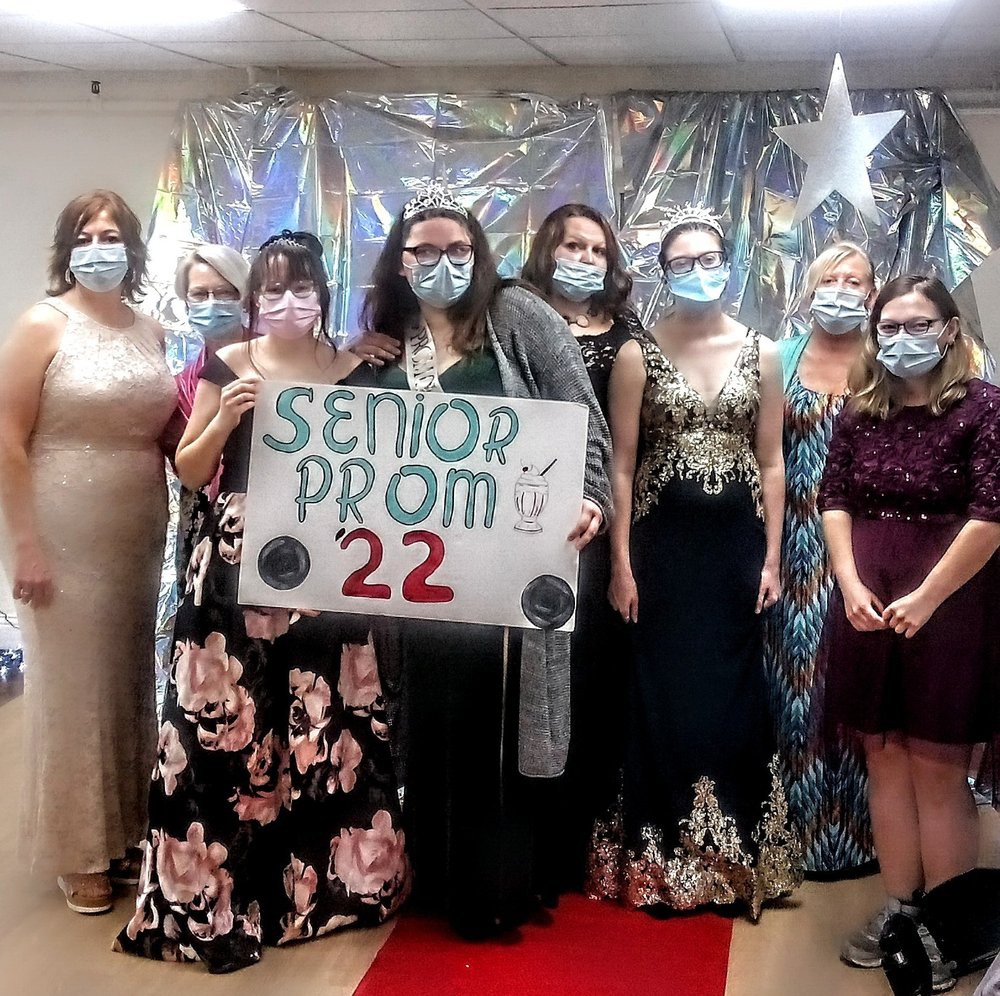 A group of people dressed in formal attire at a senior prom event, holding a sign labeled 'Senior Prom 22'.