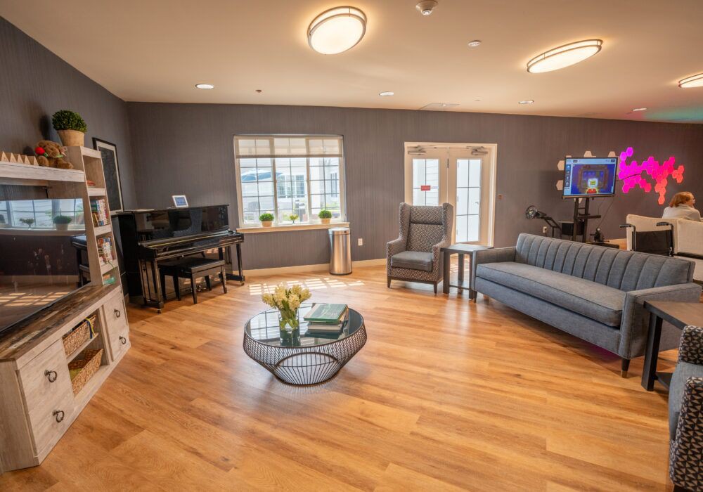 A cozy living room with a wooden floor, featuring a sofa, armchair, coffee table, and piano.