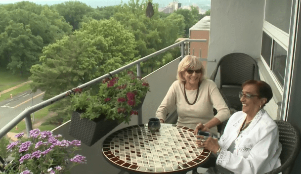Two people sitting at a table on a balcony with plants in the background.