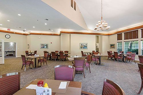 A spacious dining area with multiple tables and chairs, featuring a chandelier and wall art.