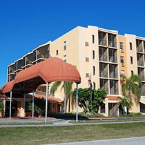 A modern apartment building with a prominent entrance and surrounding palm trees.