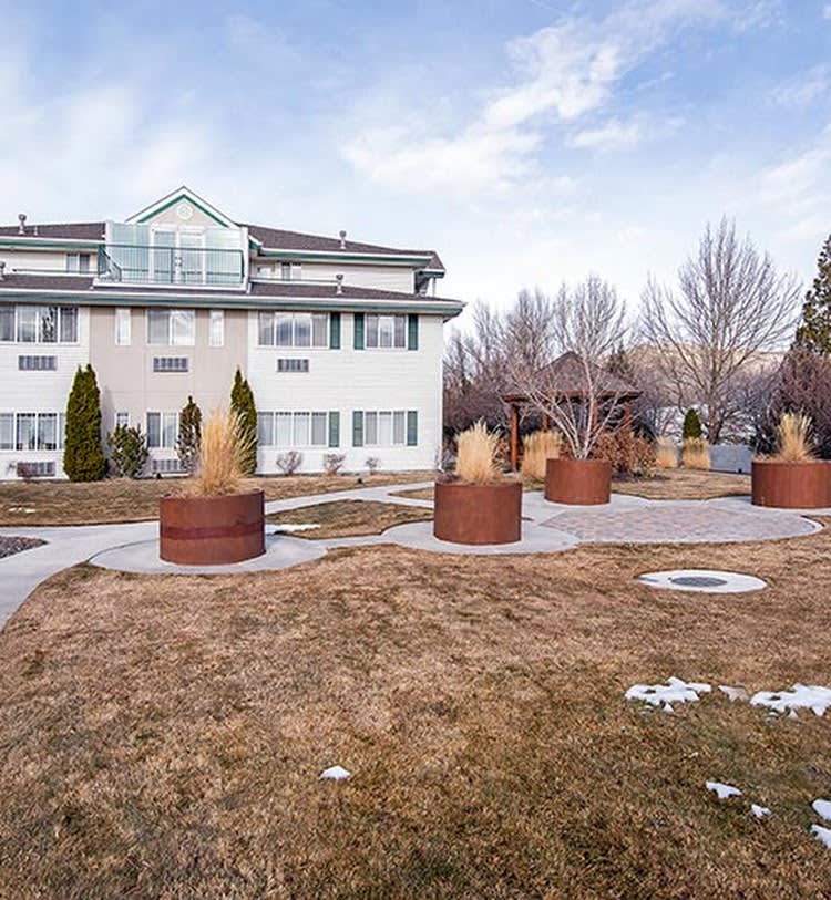 An apartment building with landscaped grounds, featuring large potted plants and bare trees under a cloudy winter sky.
