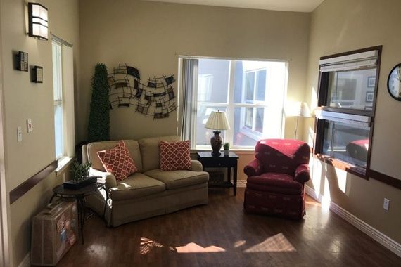 A cozy living room with a sofa, armchair, and ample natural light streaming through a large window.