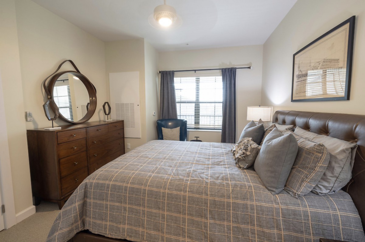 A cozy and well-decorated bedroom featuring a comfortable bed, a dresser with a mirror, and curtains framing the window.