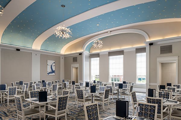 An elegant and modern conference room with a blue arched ceiling and chandeliers, set up for a professional meeting.