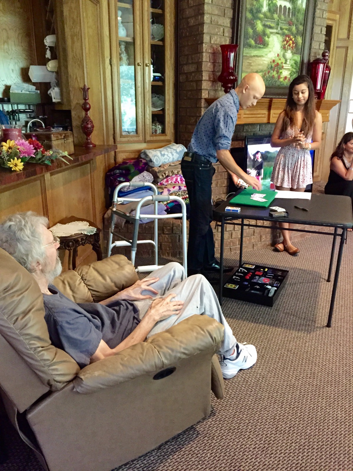 A family gathering in a living room, with an elderly person seated and others standing nearby.