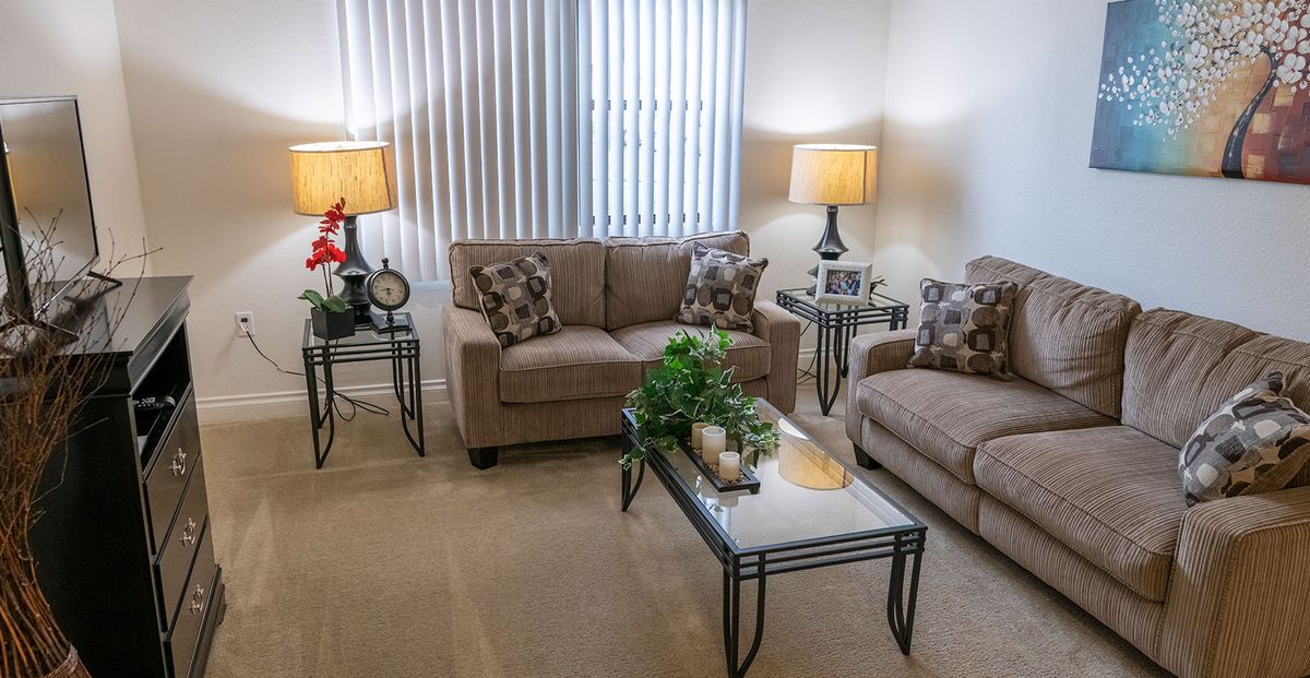 A cozy living room with neutral tones featuring a sofa set, coffee table, and indoor plants.