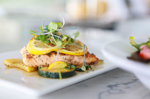 A beautifully plated salmon dish topped with fresh lemon slices and microgreens.