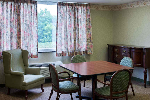 A cozy room featuring a wooden table surrounded by chairs, with floral curtains letting in natural light.