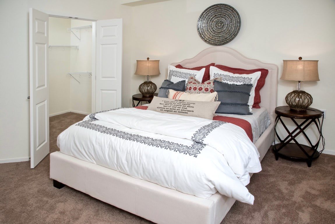 A neatly arranged bedroom with a stylishly decorated bed, featuring pillows and a bedside lamp.