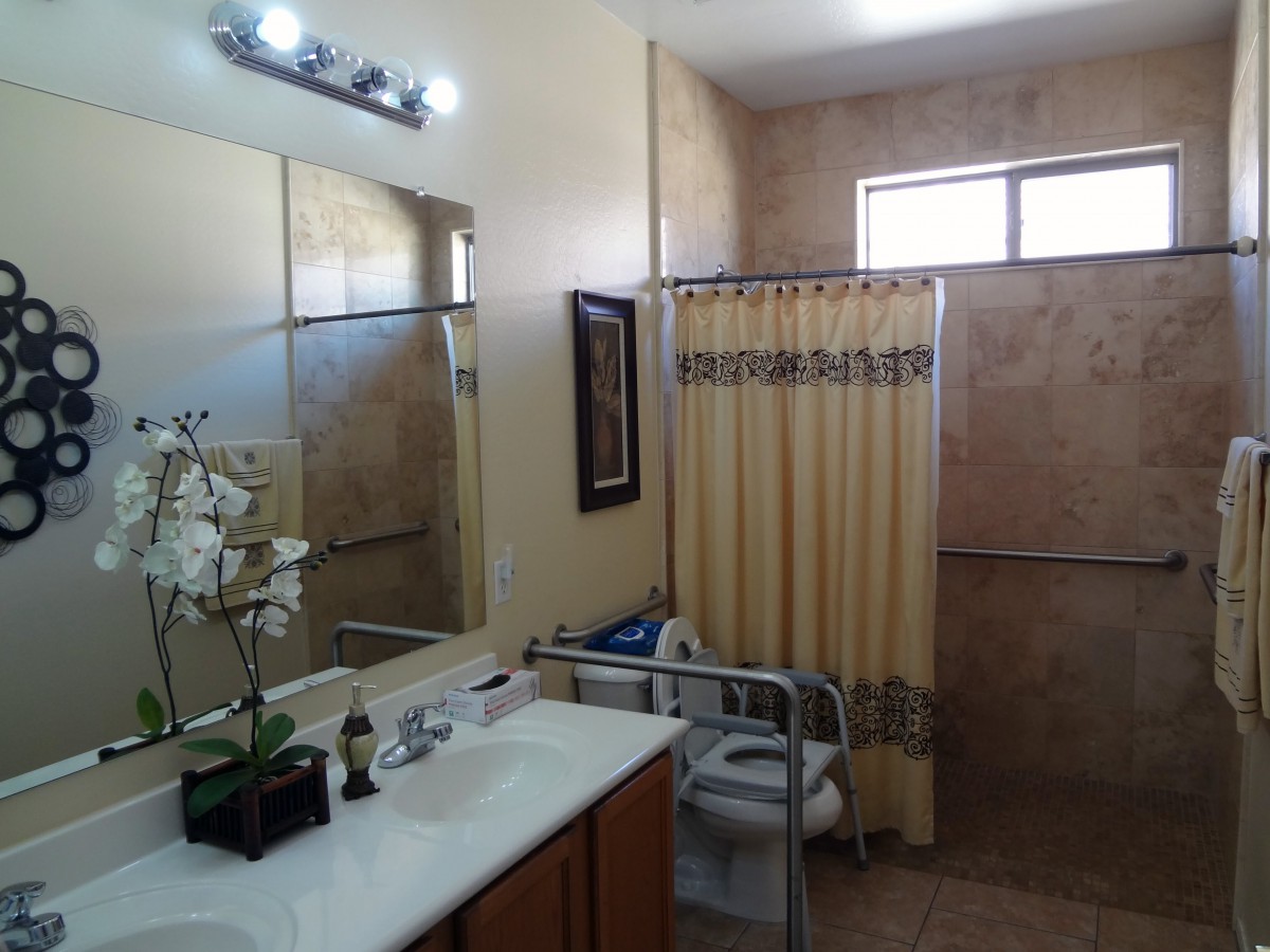 A well-lit bathroom featuring a large mirror, sink, handrails for accessibility, and a shower with a curtain.