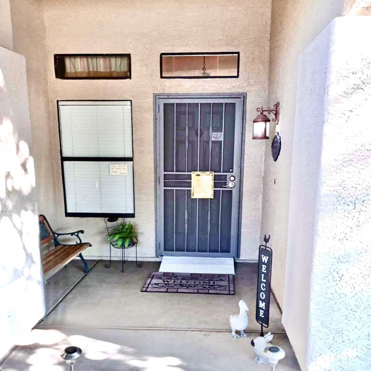 A cozy front porch area with a secure metal door, a bench, and a potted plant.