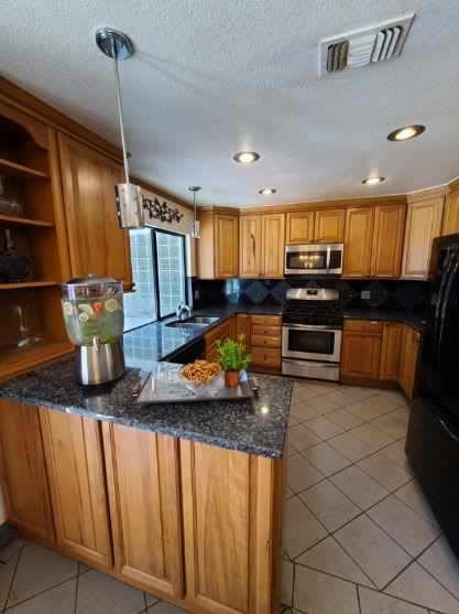 A modern kitchen with wooden cabinets and granite countertops, featuring a double oven and ample natural light.