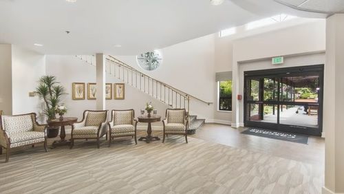 A spacious lobby featuring a seating area with elegant chairs, a staircase, and an entrance door.