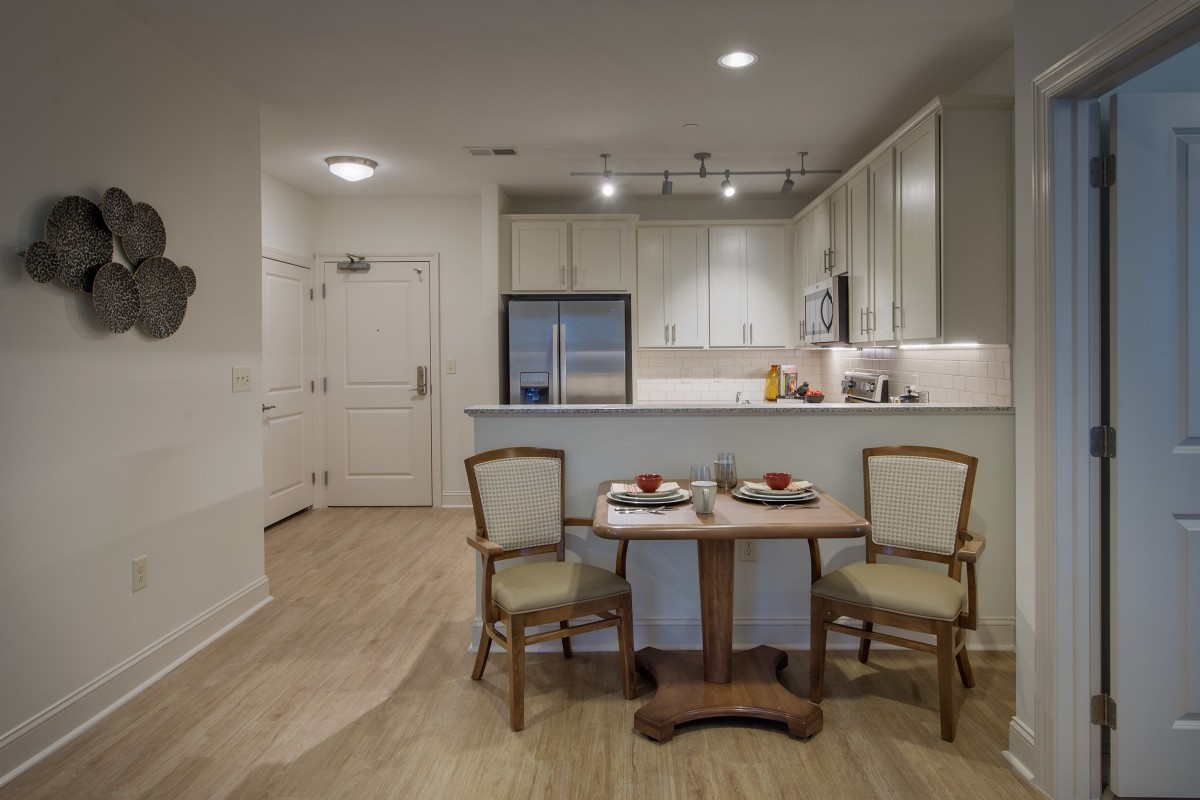 A modern kitchen with a small dining table and chairs, featuring appliances and a minimalist design.