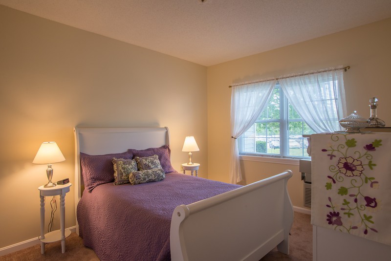 A cozy bedroom with purple bedding and warm lighting.