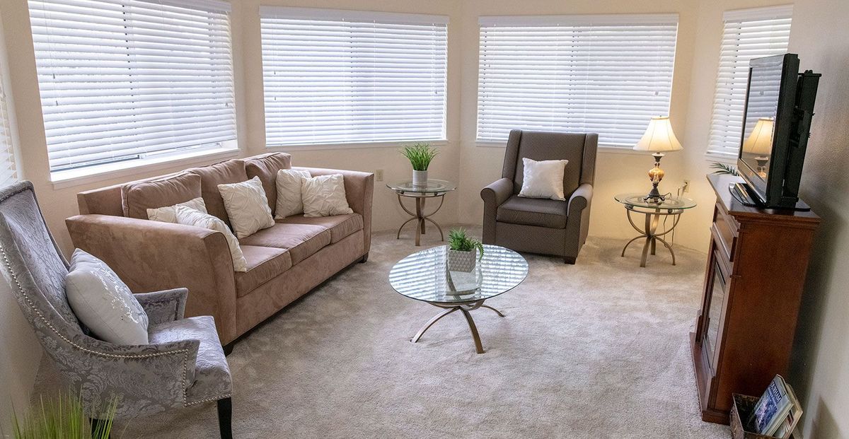 A cozy living room with a sofa, armchair, and glass coffee table, featuring neutral colors and decor.