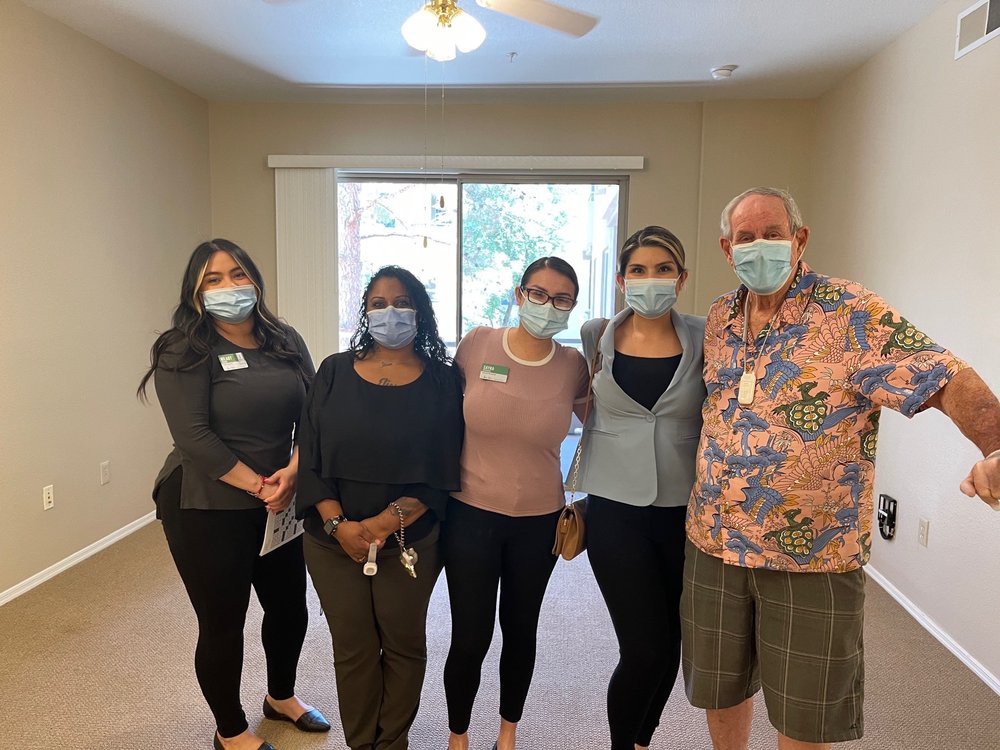 A group of five people wearing masks posing together in a room.