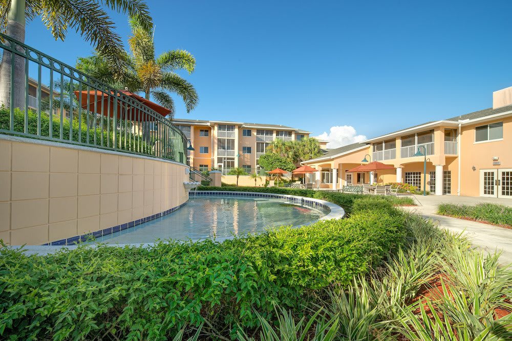 A scenic view of a tropical resort featuring a pool, lush greenery, and palm trees under a clear blue sky.