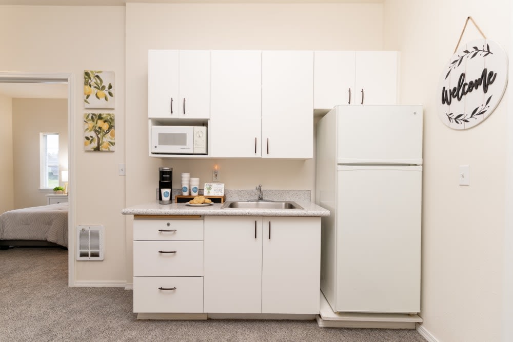 A compact kitchen setup featuring white cabinets, a refrigerator, microwave, and a sink.