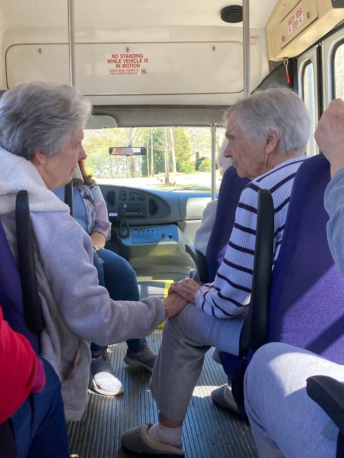 Two elderly individuals engage in conversation while traveling on a bus.