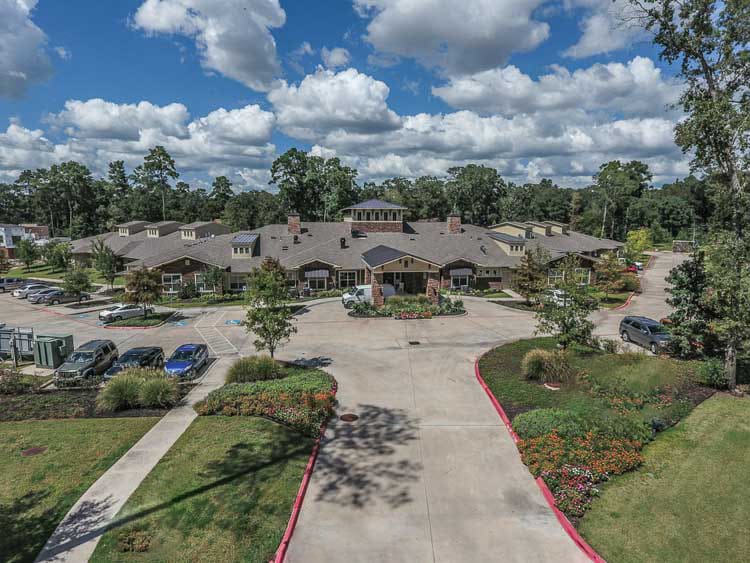 Aerial view of a large building surrounded by landscaped gardens and a parking area under a partly cloudy sky.
