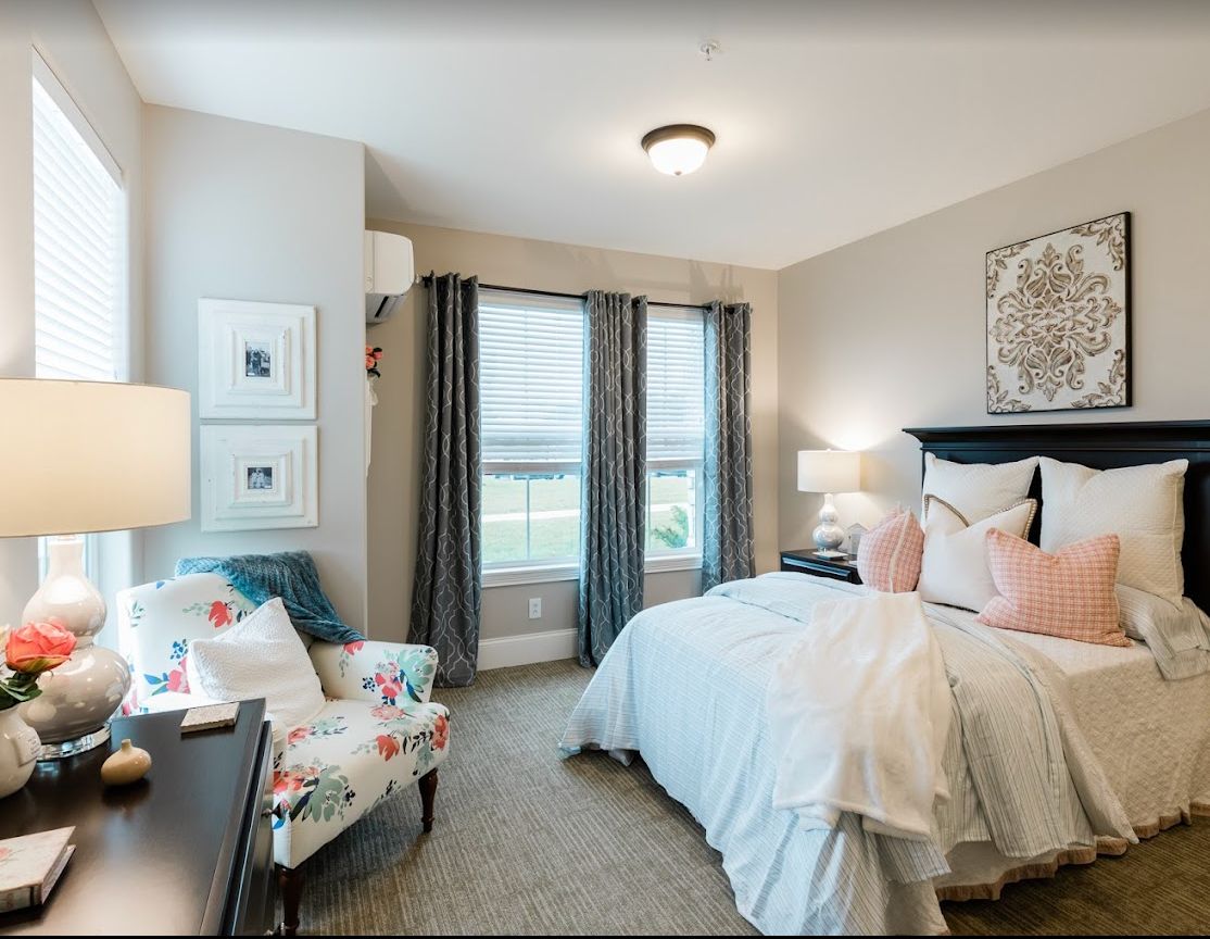 A cozy and well-decorated bedroom with a bed, armchair, lamps, and large windows.