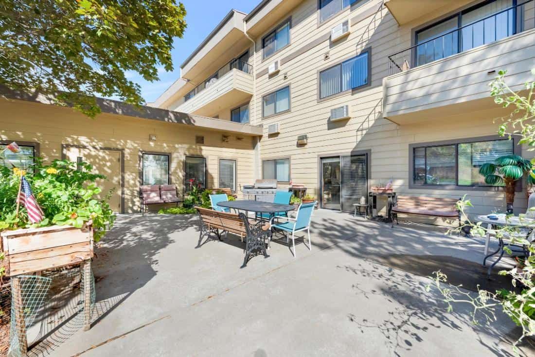 A sunny outdoor patio area at an apartment building, featuring seating and plants.