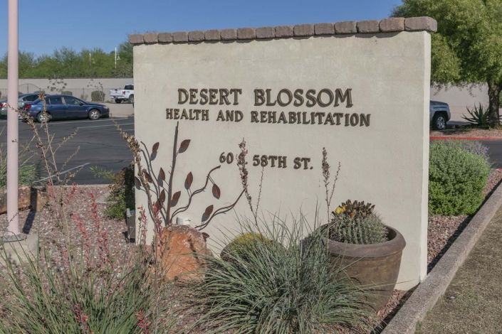 Sign for Desert Blossom Health and Rehabilitation with desert plants in the foreground.