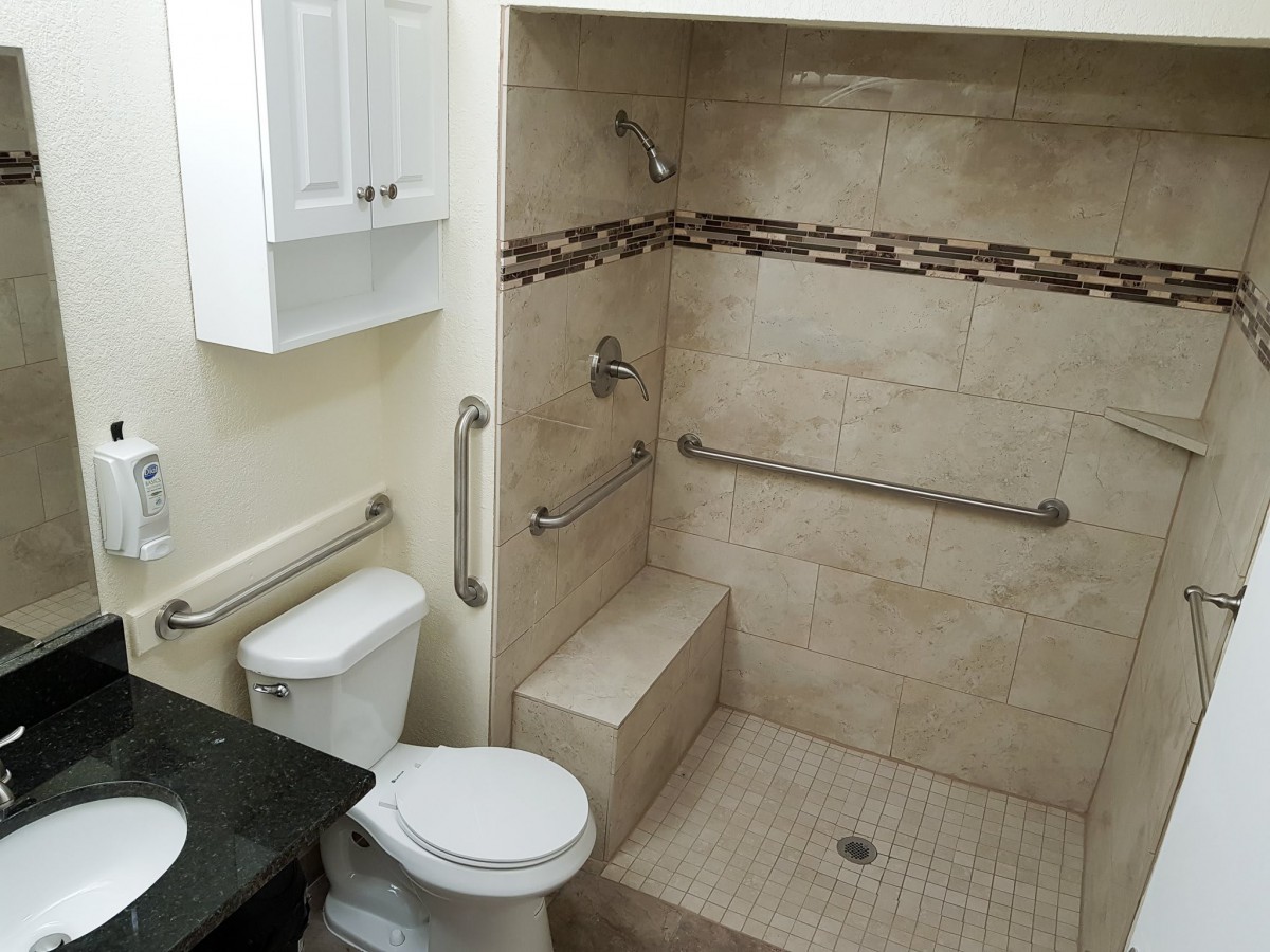 A bathroom with an accessible shower, featuring grab bars and a built-in shower seat.