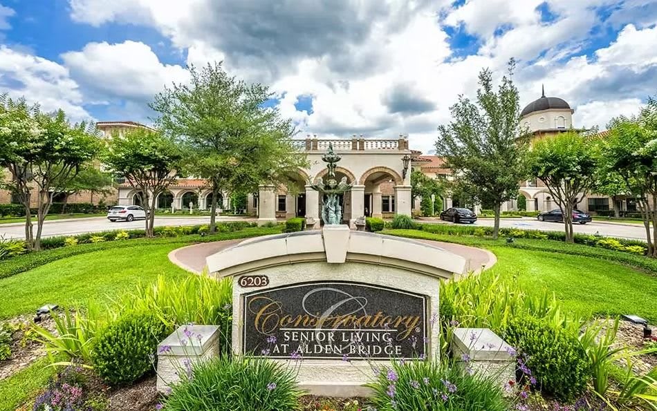 View of a luxury residential building with well-maintained gardens and a decorative sign in the foreground.