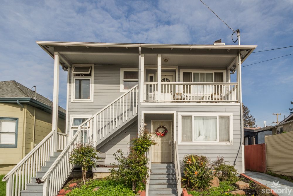 A two-story residential house with a porch and stairs leading to the entrance, surrounded by a small front yard.