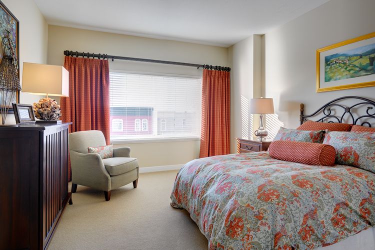 A cozy bedroom featuring a colorful bedspread, an armchair, and red curtains.