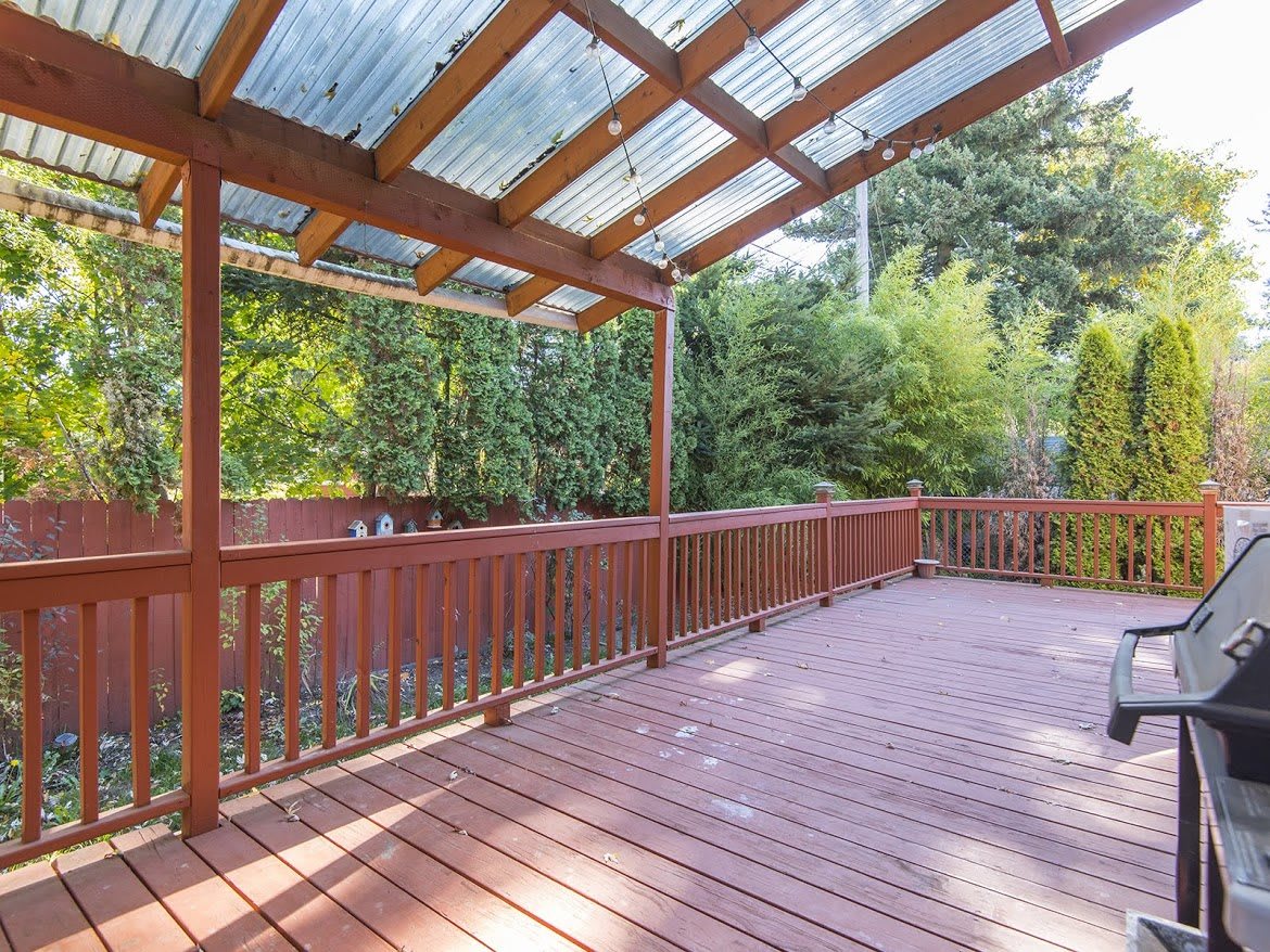 A spacious wooden deck with a pergola roof, overlooking a lush garden.