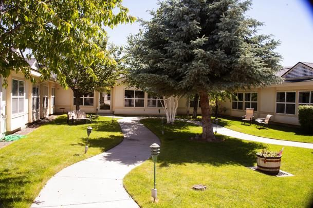 A scenic garden pathway leading to a residential building surrounded by lush trees and a well-maintained lawn.
