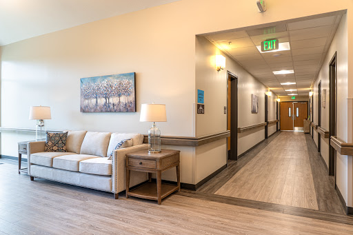 A well-lit hallway featuring a cozy lounge area with a sofa, lamp, and contemporary artwork.