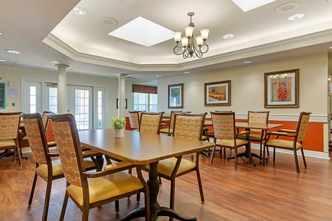 A well-lit dining room featuring wooden tables and chairs, decorative paintings, and a chandelier.