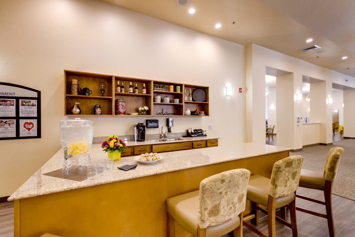 A modern kitchen interior with a counter, bar stools, and a coffee station.