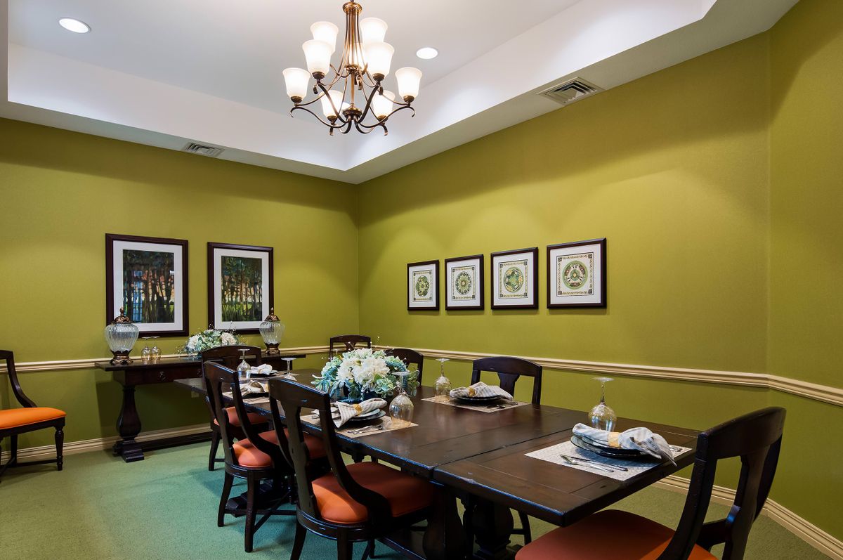 A stylish dining room with green walls, featuring a chandelier, a large dining table, and decorative wall art.